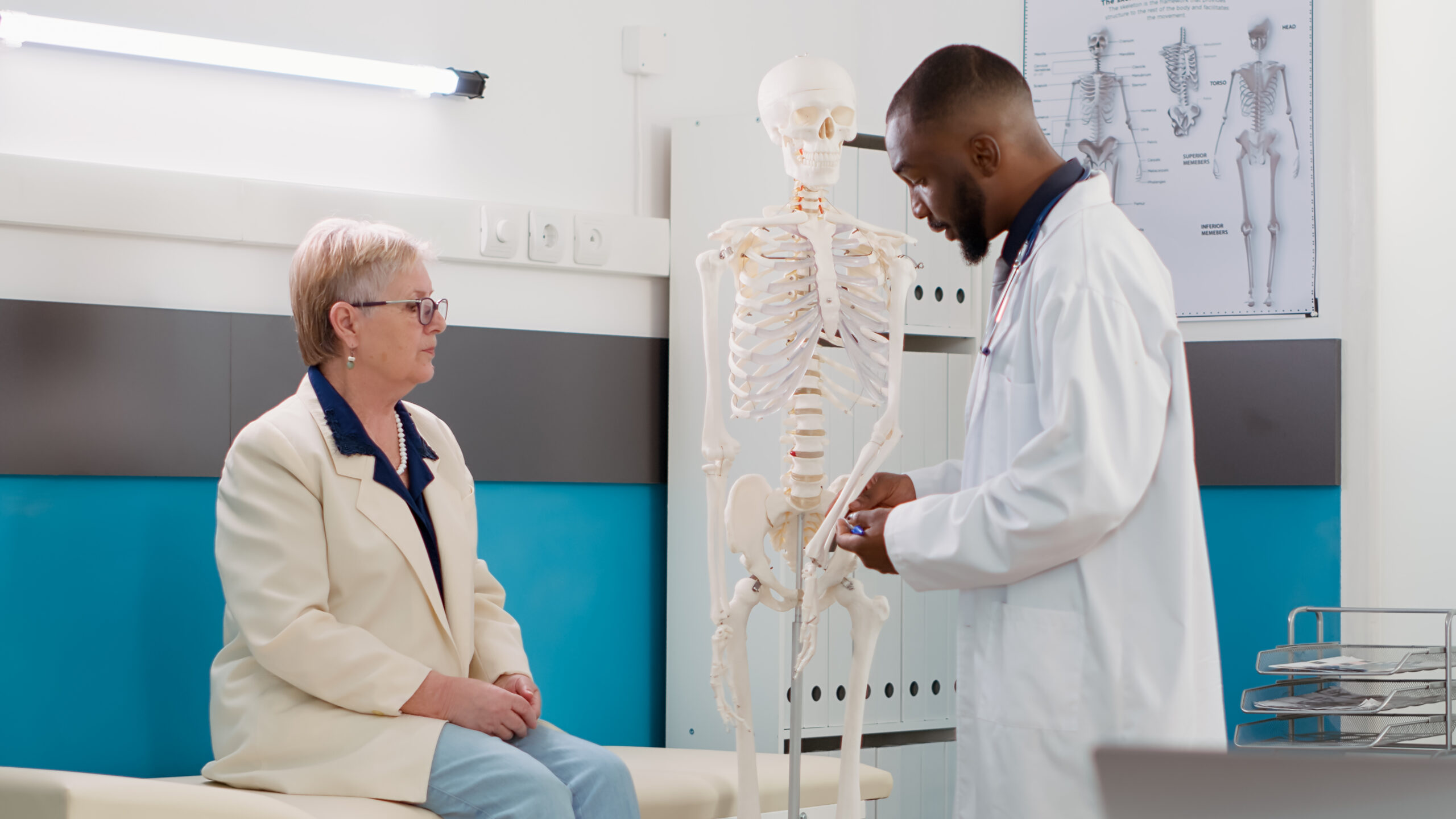 Orthopäde zeigt einer älterten Patientin den Unterarm eines Skelett-Modell