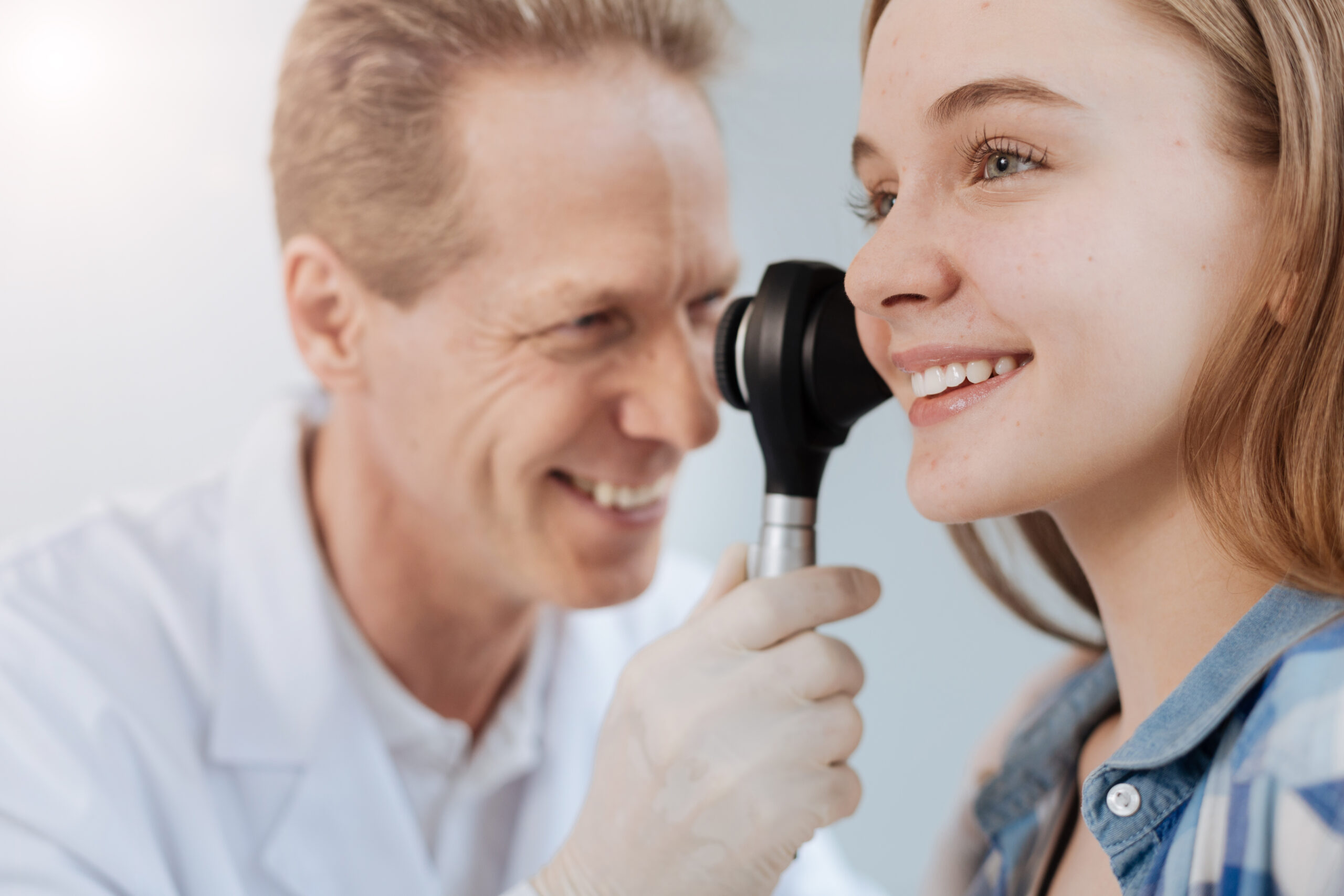 Arzt untersucht mit einem Gerät das Ohr einer lächelnden Frau